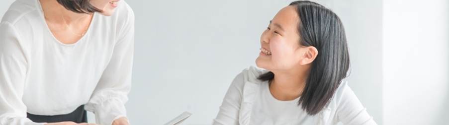 机に座って勉強する女子生徒と、それに笑顔で話しかける女性講師の写真