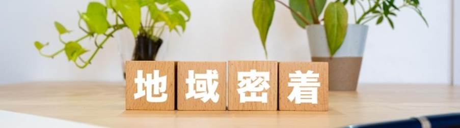 観葉植物と地域密着の文字が描かれた木製ブロックの温かみあるイメージ